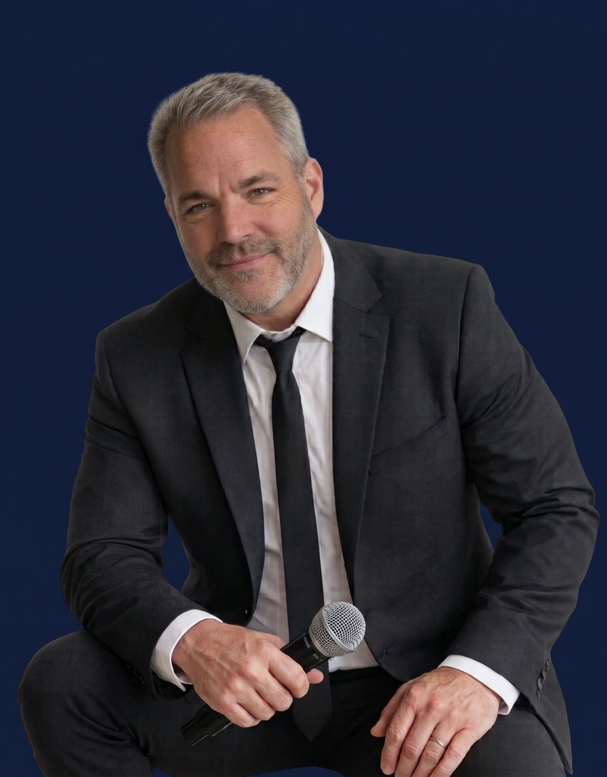 Comedian Mike James smiling in a dark suit and tie, holding a microphone